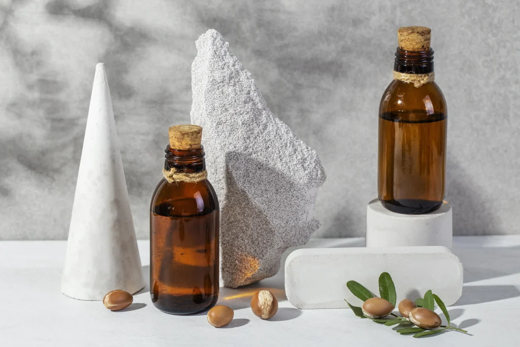 A modern product setup with amber argan oil bottles, concrete stands, and argan nuts.