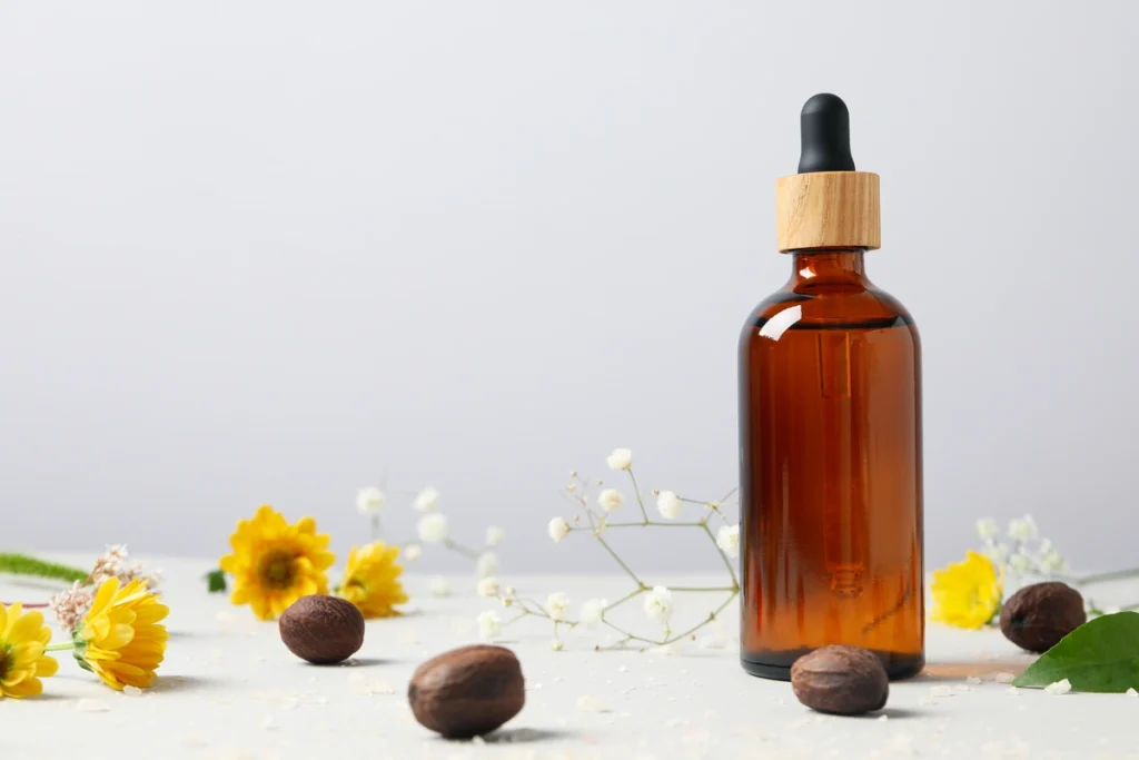An amber dropper bottle with a wooden top, surrounded by argan nuts and yellow flowers.