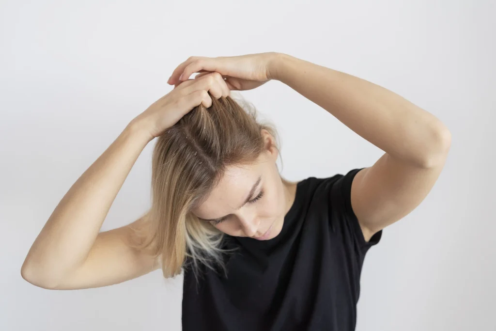 A woman checking her scalp and blonde hair for dandruff against a clean white background.