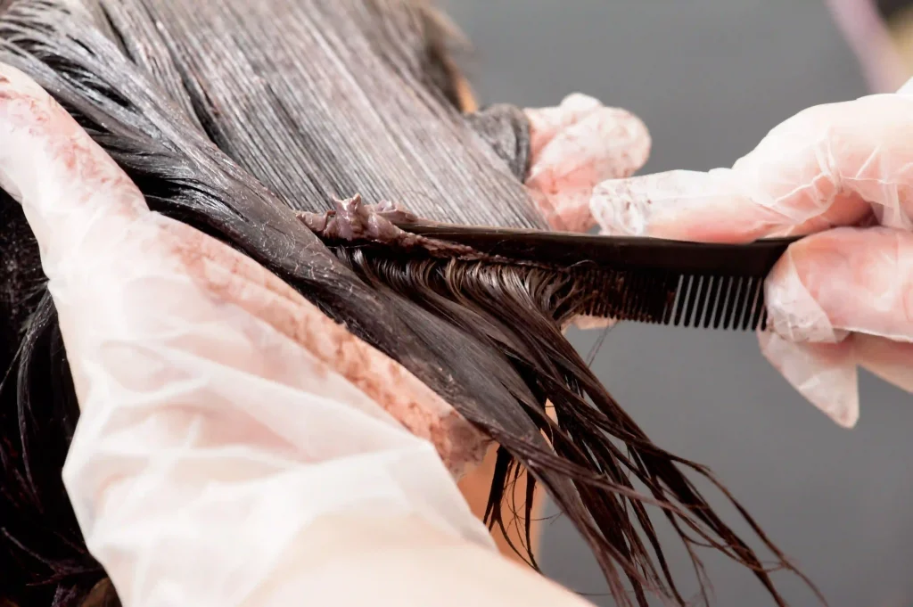 Stylist using a fine-tooth comb to ensure the keratin treatment is evenly distributed through the hair.