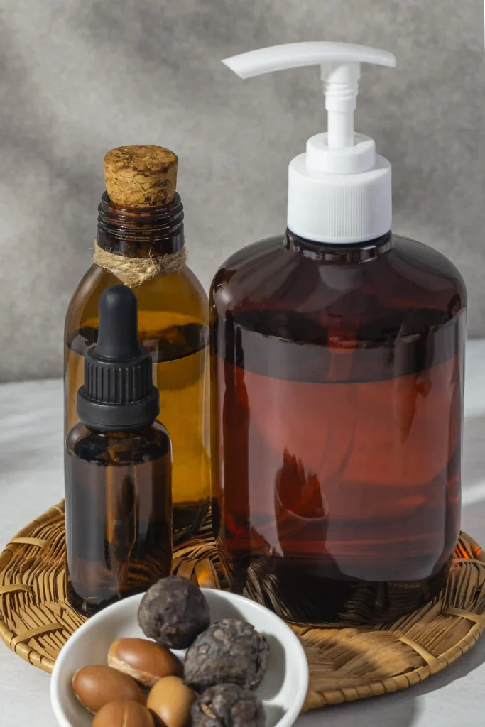 Amber glass dropper bottles and a pump dispenser next to a bowl of argan nuts and seeds.