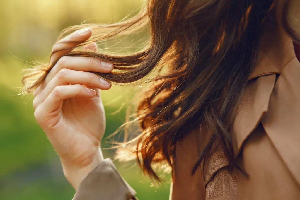 Close-up of a hand touching soft, thin brown hair illuminated by warm sunlight to show natural texture.