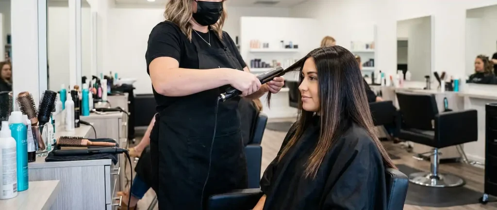 Stylist using a flat iron on small sections of straight, shiny dark hair to seal in a professional treatment.