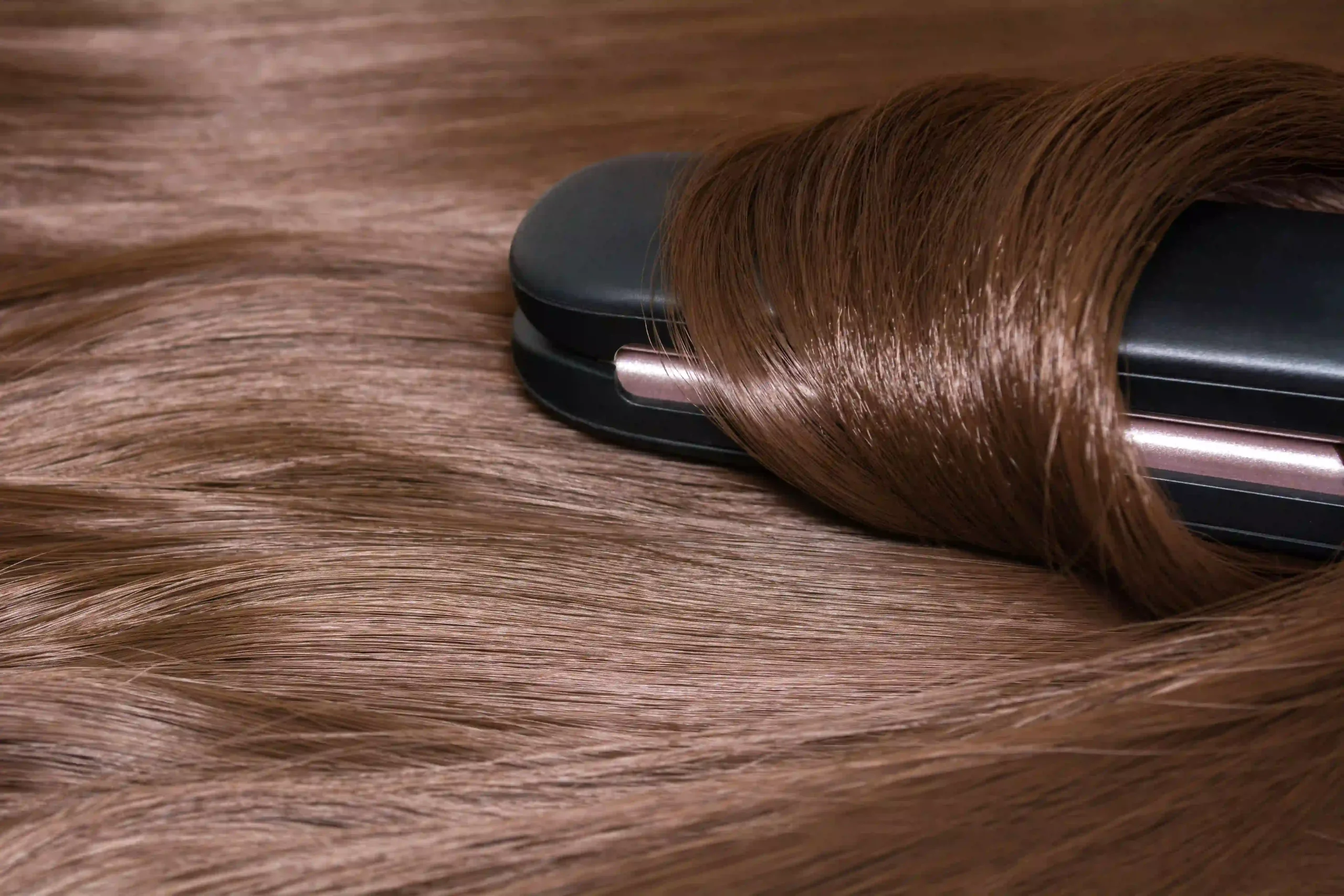 Professional hair straightener gliding through shiny, brilliant brown hair, showcasing smooth and healthy salon results.