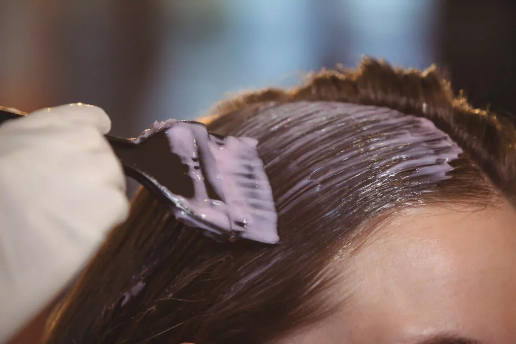 Close-up of a salon professional using a brush to apply a keratin treatment to hair sections.