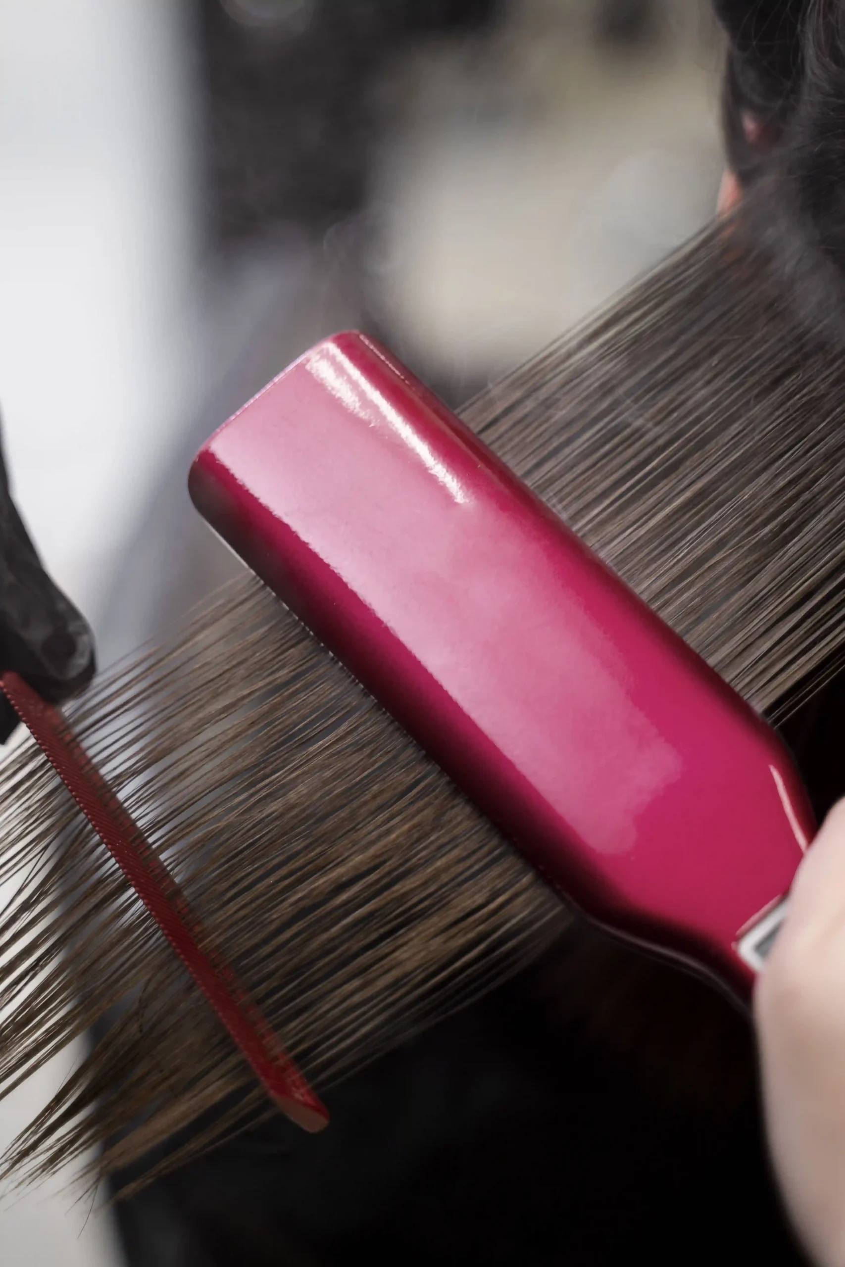 A red flat iron being used on hair to seal in the keratin treatment, creating steam and a super-smooth texture.