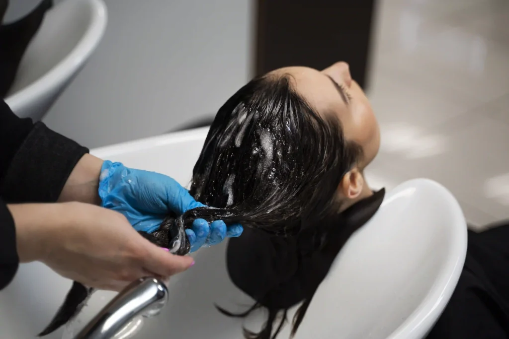 A stylist washing a client's hair at the salon basin to prepare for the keratin treatment process.