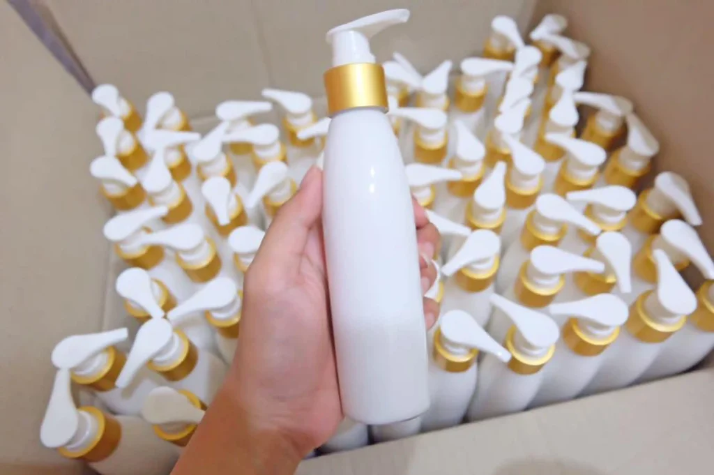 A hand holding a white pump bottle over a cardboard box filled with identical hair care products.
