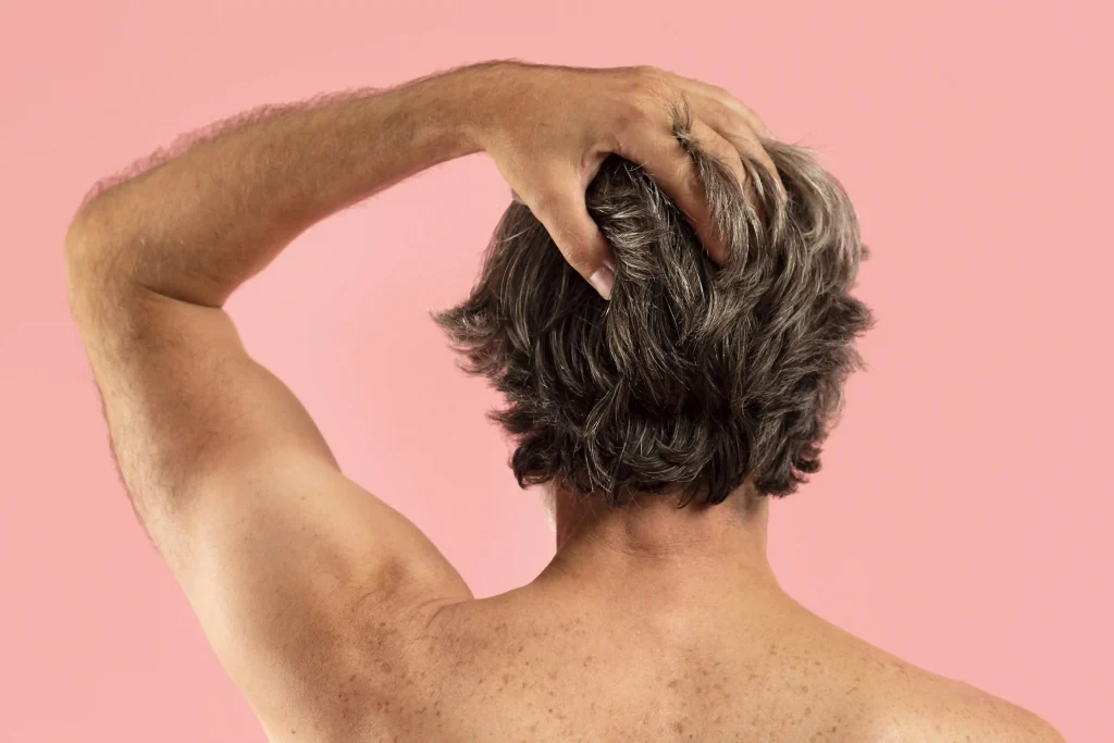 Rear view of a man with thick, textured salt-and-pepper hair against a soft pink background.