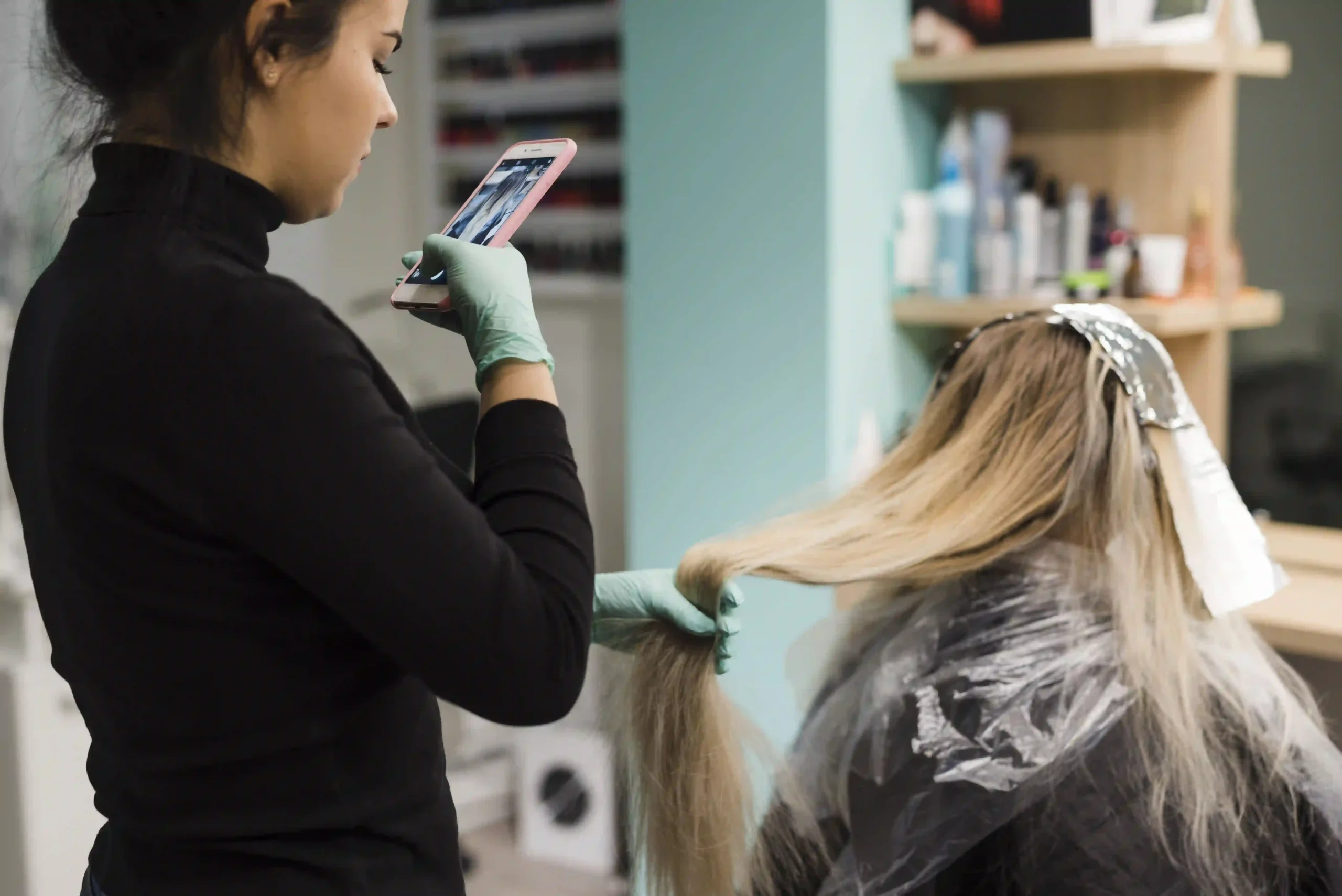 A hair stylist taking a photo of a client's hair result with a smartphone for brand social media marketing.
