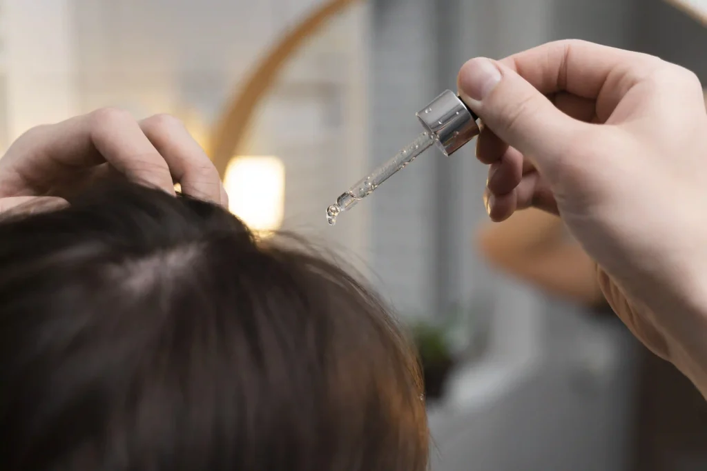 A person applying a clear liquid serum to their scalp with a glass dropper, showcasing targeted hair treatments.