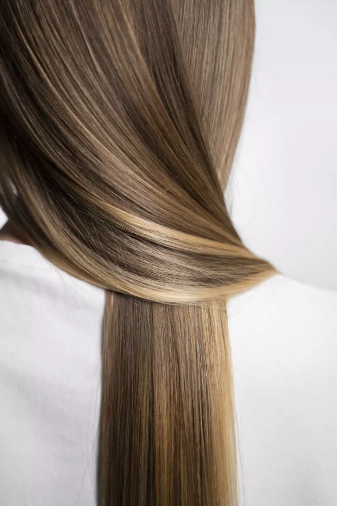 Rear view of a woman with incredibly smooth, straight, and glossy light brown hair.