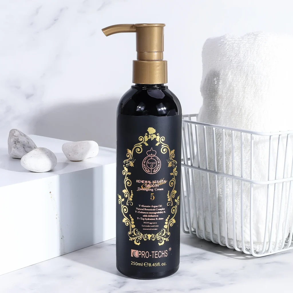 A 250ml black bottle of "Renewal Keratin Smooth Detangling Cream 5" featuring a gold pump and an ornate gold label, displayed on a marble surface next to a white basket containing a rolled towel.