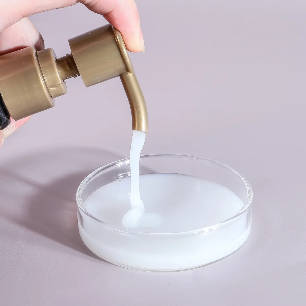 A close-up shot of a hand dispensing a creamy, opaque white "Keratin Smooth Shampoo 3" from a gold pump into a glass dish, showcasing its thick and pearlescent texture.