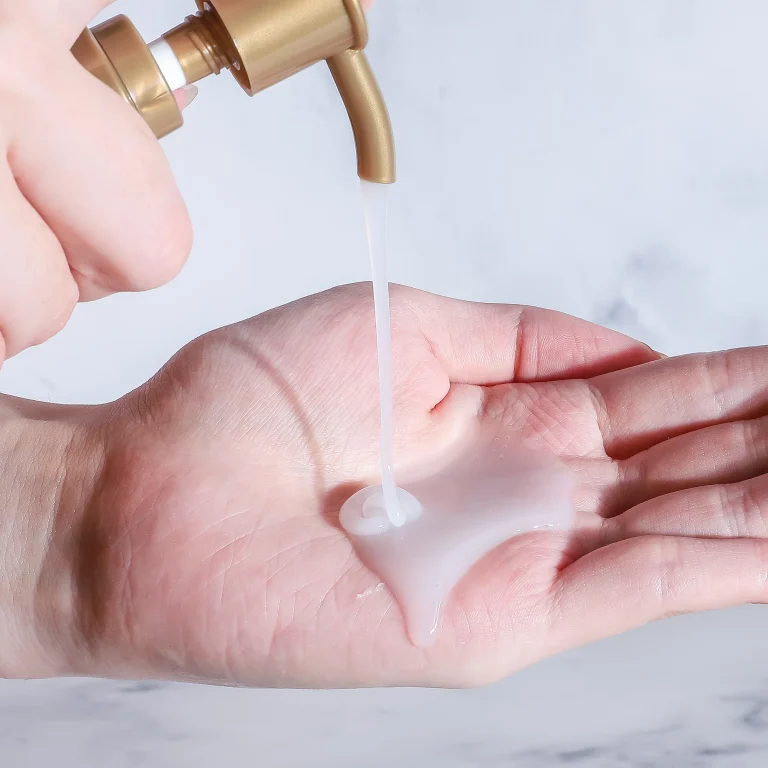 A close-up shot of a hand receiving a stream of thick, pearlescent white "Keratin Smooth Shampoo 3" dispensed from a gold pump, showcasing its smooth and creamy texture.