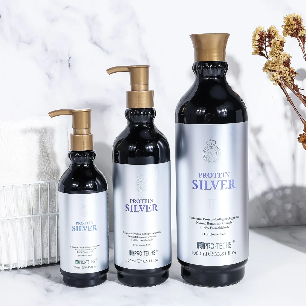Three sizes of Pro-Techs Protein Silver II hair treatment (250ml, 500ml, and 1000ml) in black bottles with silver labels and gold caps, set against a marble backdrop.