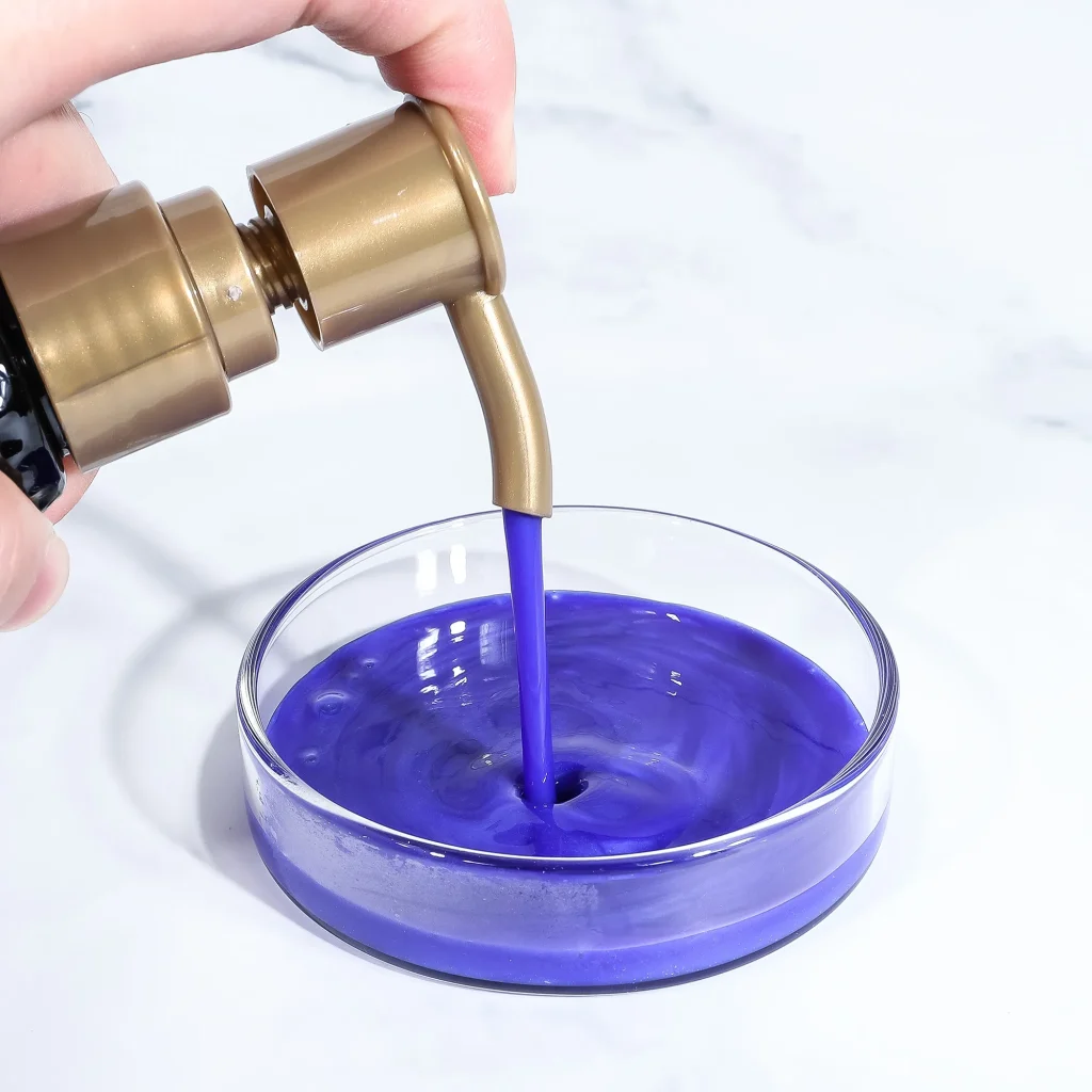 Close-up of a hand pressing a gold pump to pour vivid purple liquid into a clear glass.