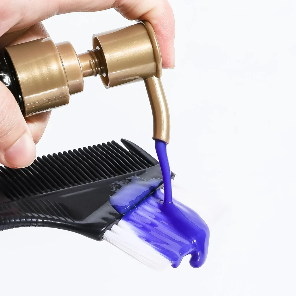 A hand dispensing a thick, vibrant purple keratin treatment from a gold pump onto a professional black hair dye brush and comb, highlighting the product's creamy texture.
