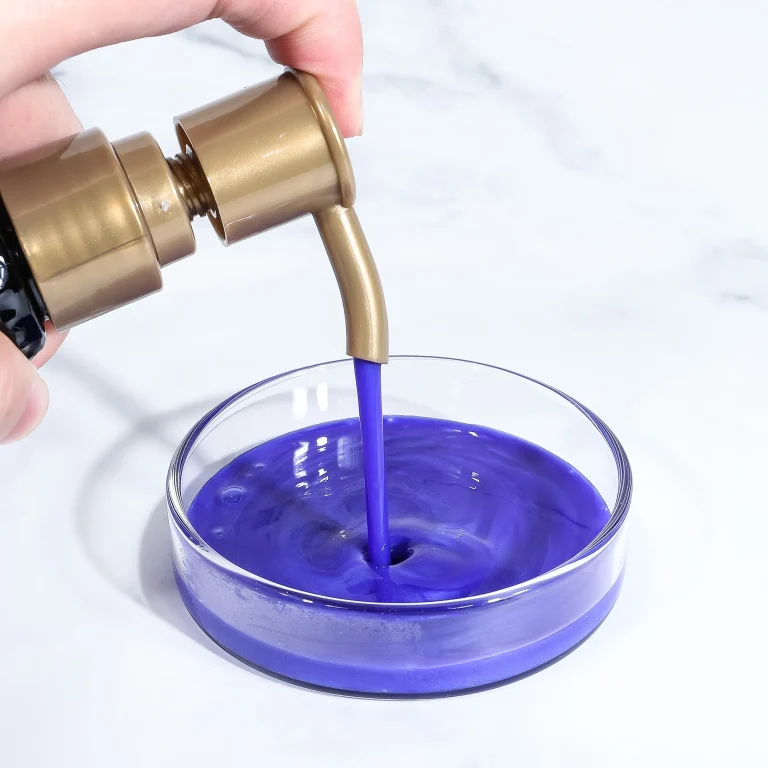 Close-up of a hand pressing a gold pump to pour vivid purple liquid into a clear glass.