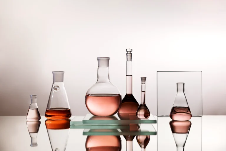 Lab glassware with pink haircare formula liquids arranged on glass shelves, reflected on the shiny surface behind them