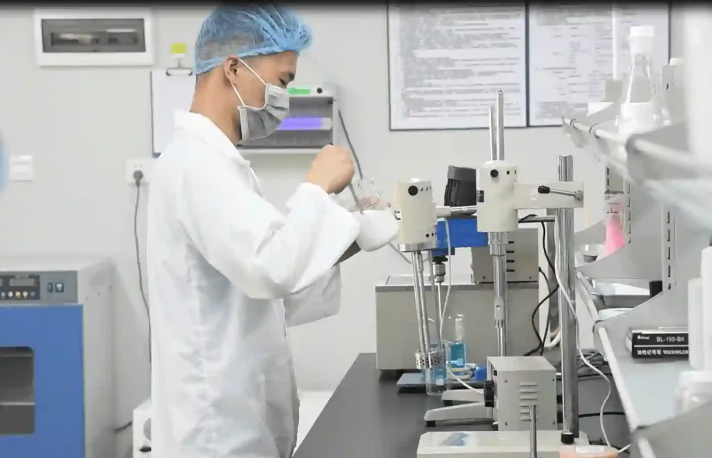 A laboratory technician in protective gear performing physicochemical stability tests on a white cream product.