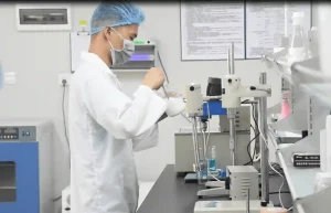 A laboratory technician in protective gear performing physicochemical stability tests on a white cream product.
