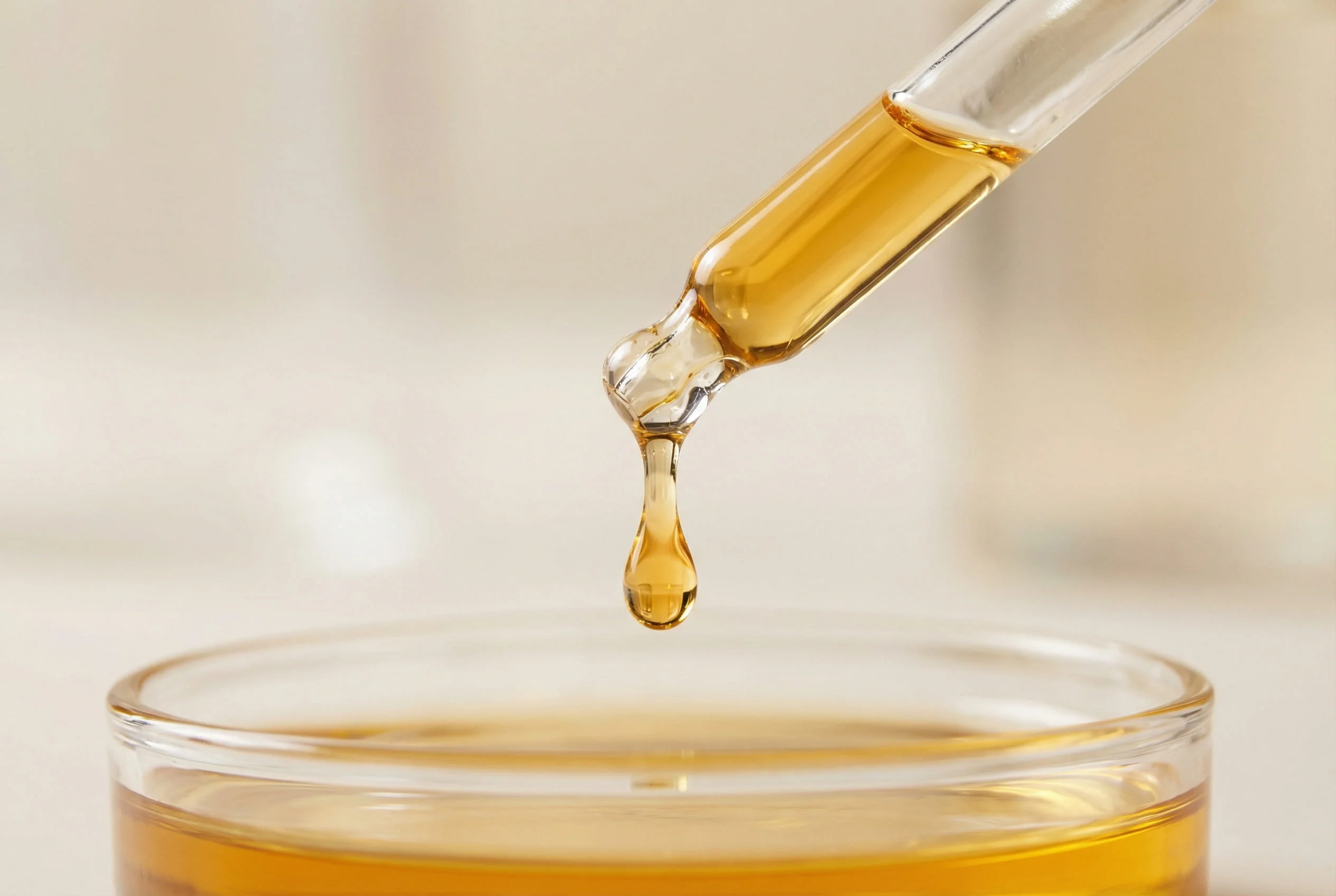 Macro shot of a golden pure Argan oil droplet from a pipette, highlighting organic hair care raw materials.