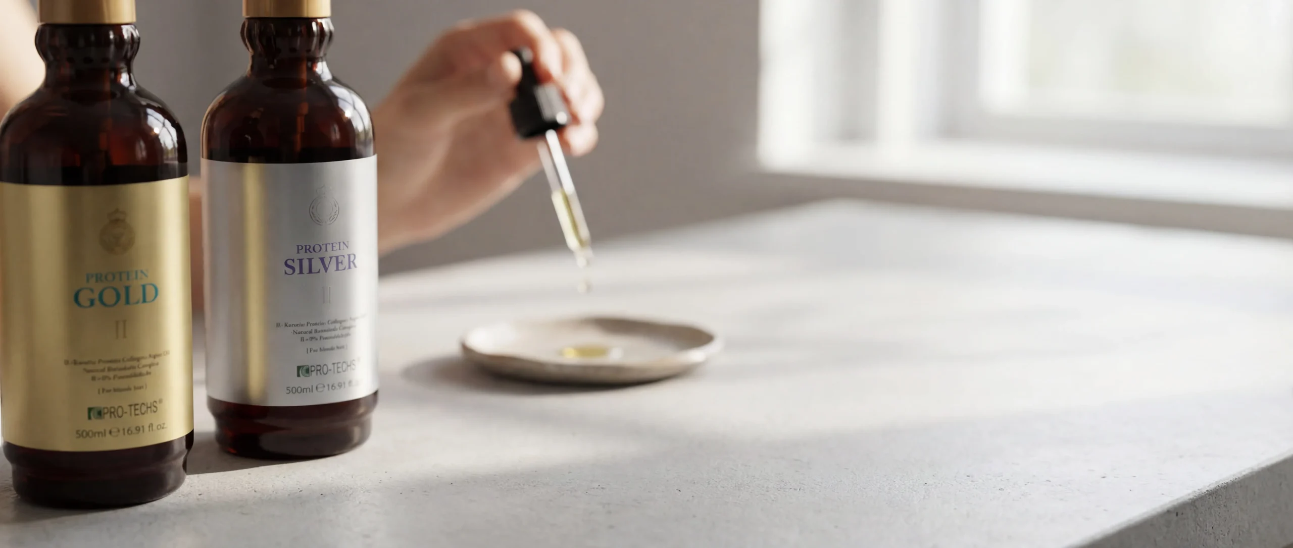 Protein Gold and Silver bottles with a serum dropper on a bright desk.
