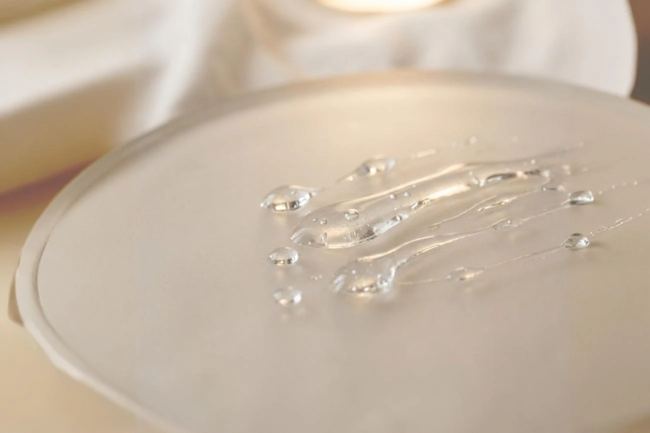 Macro shot of clear Glyoxylic Acid liquid on a frosted glass surface, a key ingredient for semi-permanent hair straightening.