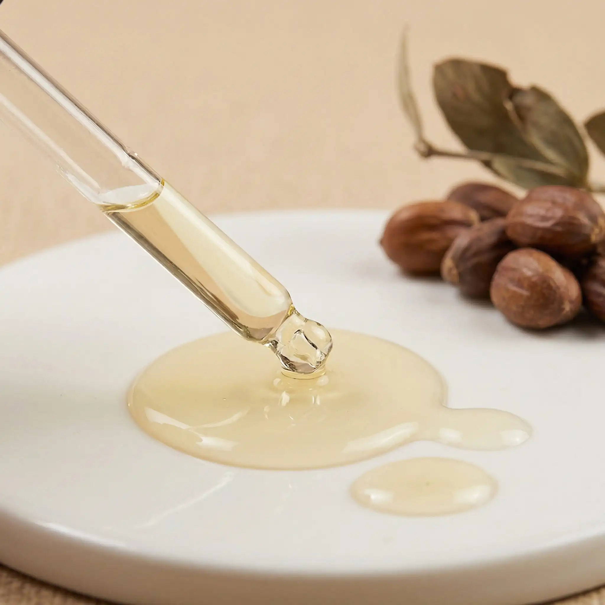 Macro shot of golden jojoba oil being dispensed from a pipette next to raw jojoba beans for premium hair formulas.