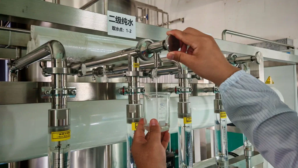 A technician collecting a water sample into a glass beaker from a stainless steel purification system.