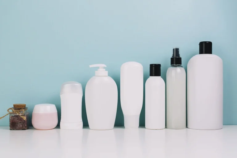 A row of assorted cosmetic and haircare containers in various shapes and sizes against a light blue background.