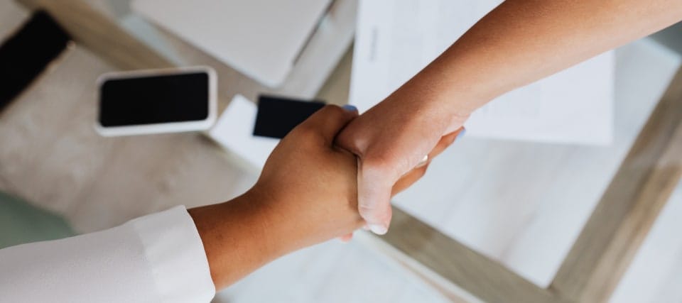 Two people shaking hands over a desk with a smartphone and papers nearby