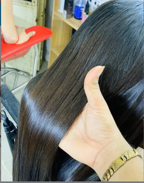 Close-up of a stylist's hand giving a thumbs-up while holding long, shiny black hair in a salon setting.