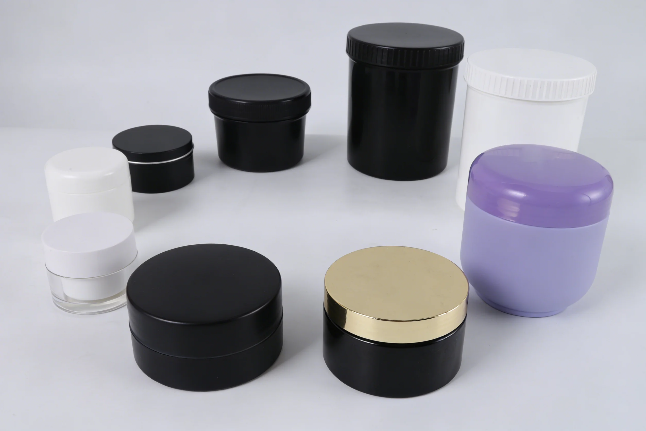 A circular arrangement of various hair mask jars in different sizes and colors, including black, white, purple, and one with a gold lid, displayed on a plain white surface.