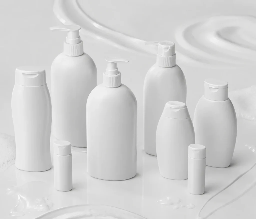 Assortment of white lotion, shampoo, and conditioner bottles arranged on a glossy bathroom surface with pumps and caps visible.