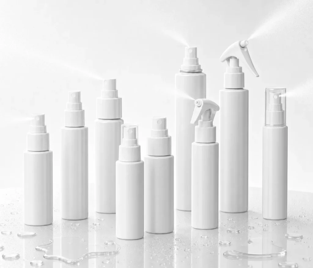 Row of white spray bottles on a reflective wet-looking surface in a studio setting.