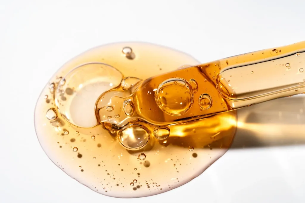 Macro shot of golden argan hair oil droplet with a glass pipette