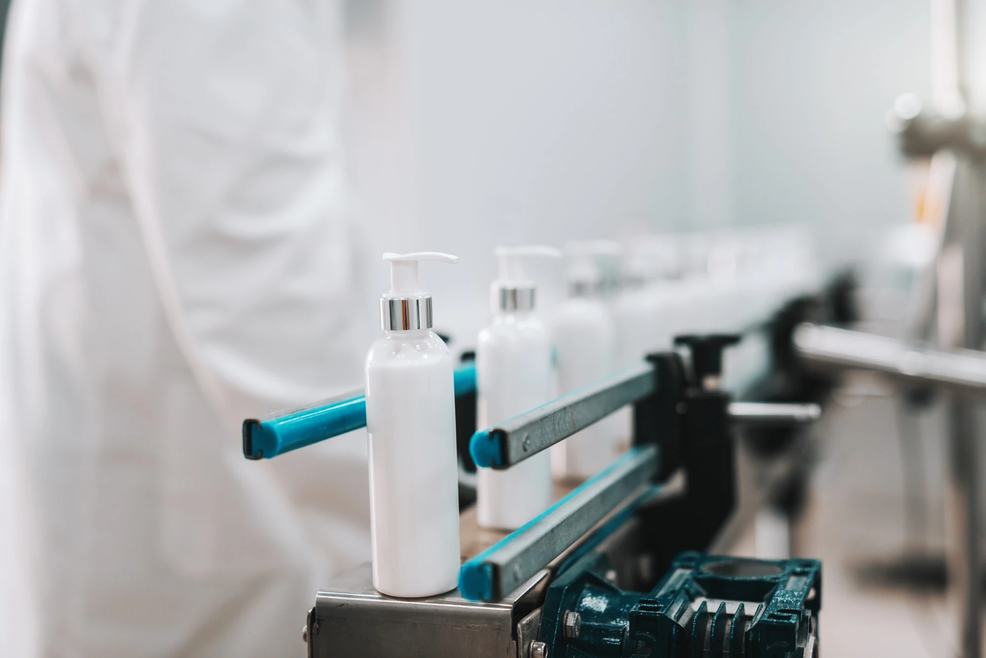 White pump bottle on a soap/hand sanitizer production line, with blue rails and blurred background of a clean industrial setting