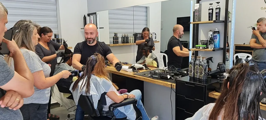 Busy hair salon scene: multiple stylists cut and style clients seated with capes, mirrors and product shelves in the background.
