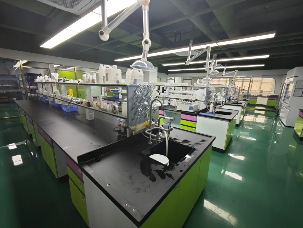 A modern science laboratory with green benches, glassware, and overhead articulating arms for experiments viewed from a long workbench.