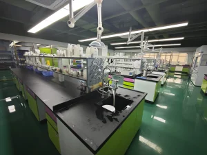 A modern science laboratory with green benches, glassware, and overhead articulating arms for experiments viewed from a long workbench.