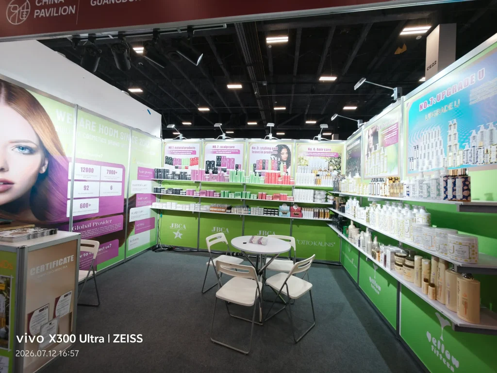 Cosmetics trade-show booth with shelves of products along the right and a large portrait banner of a woman on the left.