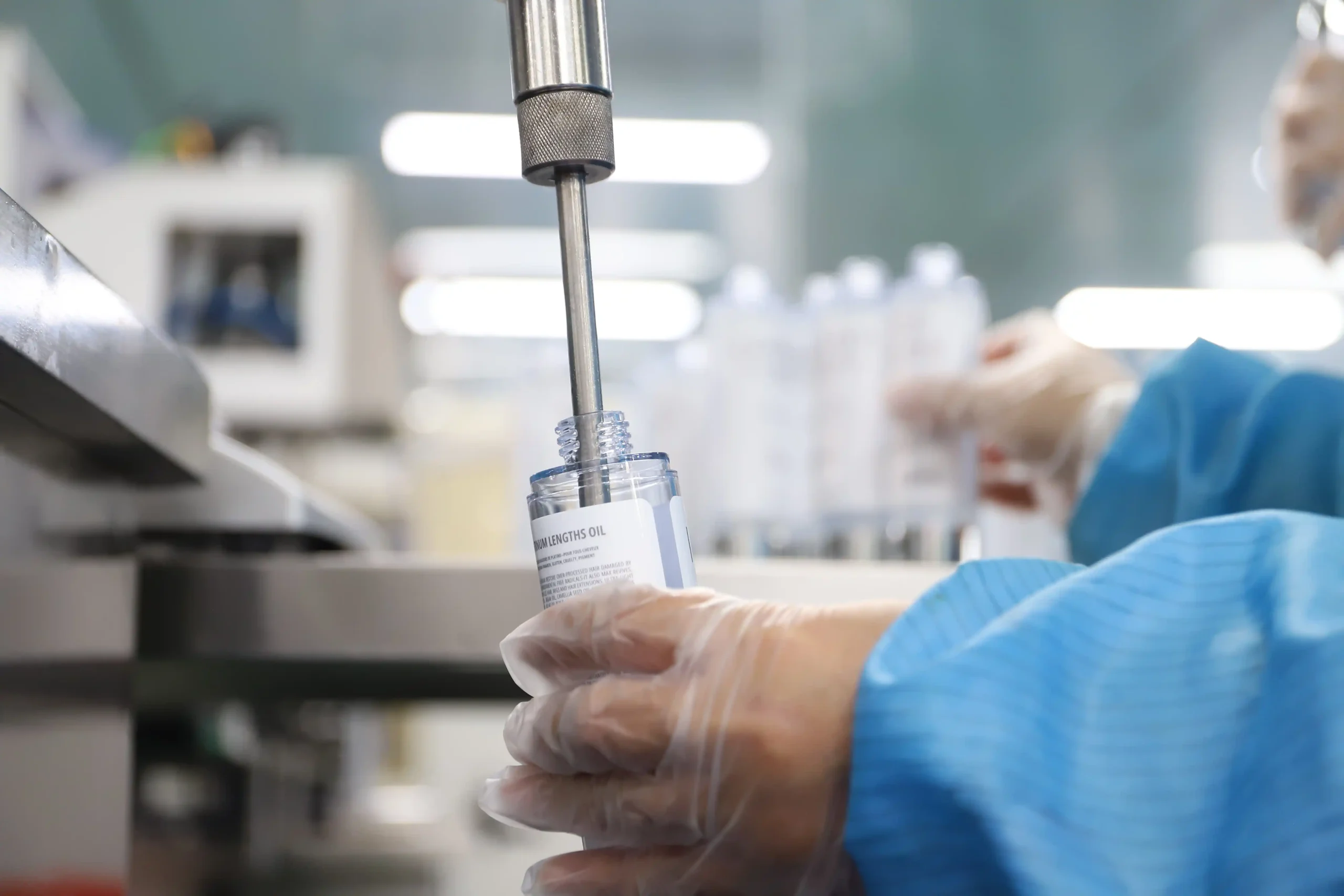 Automated liquid filling nozzle dispensing private label hair oil into clear bottles inside a cleanroom hair care manufacturing facility.