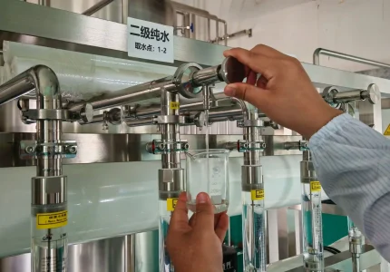 A technician collecting a water sample into a glass beaker from a stainless steel purification system.